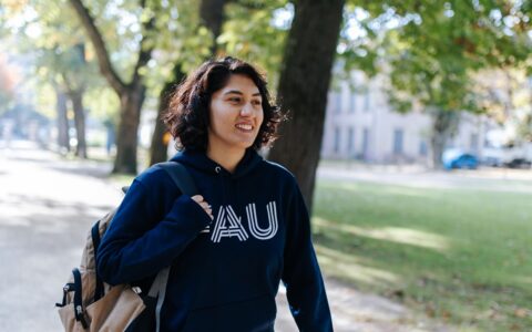 Eine junge Frau mit dunkelblauem Pullover und Rucksack läuft durch einen Park.